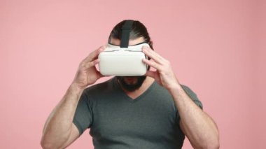 Uzun saçlı ve sakallı keyifli bir adam VR gözlüklerini çıkartıyor, yüzü pembe arka planda sevinç ve merak dolu bir ifadeye bürünüyor. Kamera 8K HAM. 