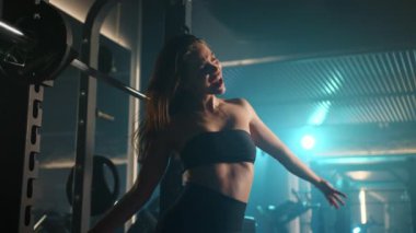 Genç bir kadın halter egzersizini dans hareketleri ve şarkı söylemeyle birleştiriyor, dinlenme araları boyunca spor salonunu sahnesine çeviriyor. Kamera 8K HAM. 