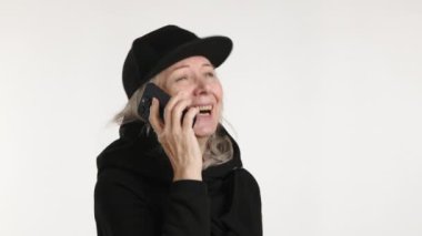 Siyah şapkalı mutlu bir kadın, bir telefon konuşmasında, kolları kapalı bir şekilde el kol hareketleriyle meşgul..