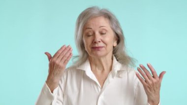 Gözleri kapalı, hoş bir son sınıf öğrencisi, elleri zarif bir şekilde havada, açık mavi arka planda hoş bir kokunun zevkine varıyor. Kamera 8K HAM. 