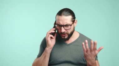 Uzun saçlı ve sakallı bir adamı, hararetli bir telefon konuşması yaparken tedirgin ve sıkıntılı bir şekilde el kol hareketi yaparken gösteren yakın plan bir resim. Kamera 8K HAM. 