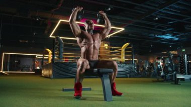 Kas geliştirici modern bir spor salonunda halterli omuz presi yapıyor neon ışıkla geliştirilmiş, fiziksel kondisyonu ve odaklanmasını en üst seviyede gösteriyor. Kamera 8K HAM. 