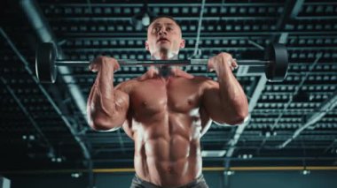 Çağdaş bir spor salonunda, kaslı bir adam halter, azim, çaba ve disiplin göstererek sağlıklı bir spor salonu rutini için gücünü ve uygunluğunu gösterir.