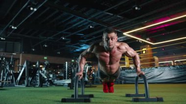 Çağdaş bir fitness merkezinde, bir adam fiziksel refahı ve dayanıklılığı vurgulayarak, paralellikleri kullanarak sıkı şınav çekerek sağlığa olan bağlılığını gösterir.