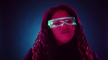 Dijital LED gözlük takan bir kadın, yüksek teknoloji ve moda anlayışıyla fütürist ve stil punk görünümünü somutlaştıran neon ışıklı arka plan karşısında görülüyor.