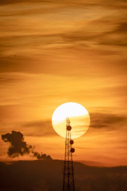 Sihouette of telecommunication pole or satellite radio station tower with big sun background