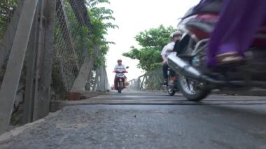 Motosikletler, nehirden karşıya geçerken geçici köprü, tehlike ve demir parmaklıklı eski köprü ve ahşap zemin yağmurlu günlerde çok güvensiz Ben Tre, Vietnam