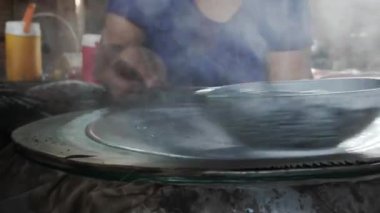 Vietnamlı kadın pirinç unundan pirinç kağıdı ya da banh trang yapıyor, dumanlı kömür ocağı el yapımı kek için yükseliyor, Ben Tre, Vietnam