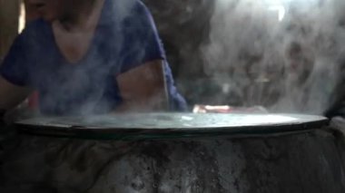 Vietnamlı kadın pirinç unundan pirinç kağıdı ya da banh trang yapıyor, dumanlı kömür ocağı el yapımı kek için yükseliyor, Ben Tre, Vietnam