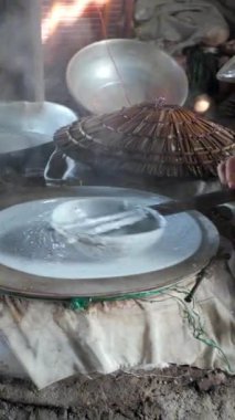 Vietnamlı kadın pirinç unundan pirinç kağıdı ya da banh trang yapıyor, dumanlı kömür ocağı el yapımı kek için yükseliyor, Ben Tre, Vietnam