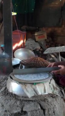 Vietnamlı kadın pirinç unundan pirinç kağıdı ya da banh trang yapıyor, dumanlı kömür ocağı el yapımı kek için yükseliyor, Ben Tre, Vietnam