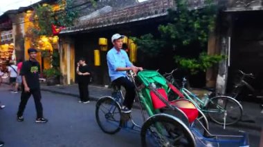 HOI AN, VIET NAM - 18 HAZİRAN 2024: Hoian antik kentinde kalabalık insanlar alacakaranlıkta, turist seyehat şehirleri bisiklet veya çocuk arabaları, yaz tatilinde renkli ışık manzarası, harika bir klasik miras