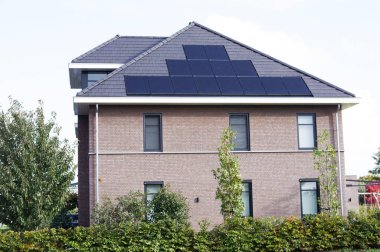 Hollanda 'daki Elst şehrinde elektrik üretimi için güneş panelleri olan kahverengi çatılı bir ev.