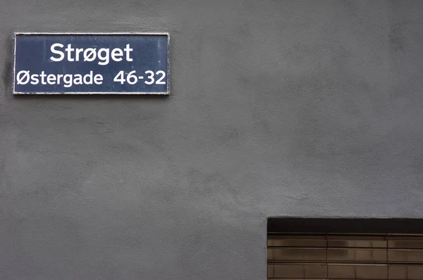 Blue street name sign of Stroget on a black stone wall in Copenhagen in Denmark. Strget is a famous shopping street in the center of Copenhagen