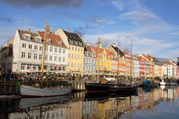 stock image Copenhagen, Denmark- April 5, 2023: Panoramic view of Nyhavn in the center of Copenhagen with colorful buildings, docked ships in the channel and people enjoying on a terrace