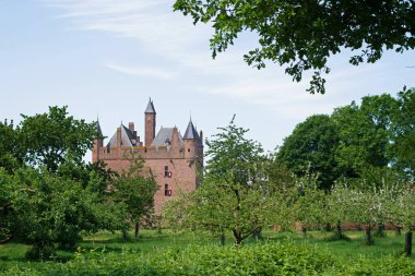Hollanda, Doornenburg 'daki ağaçlar arasında ortaçağ şatosu. Mavi gökyüzü ve bulutlar.