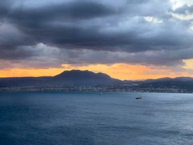 Gün batımında bulutlu gökyüzüne karşı deniz manzarası ve siluet sıradağları