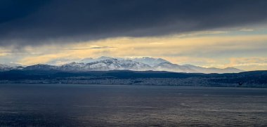 Gün batımında bulutlara karşı deniz manzarası ve karla kaplı dağ manzarası