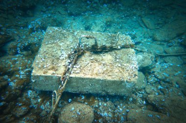 Yüksek açılı halat ve zincir manzarası, mavi denizin altındaki beton bloğa bağlanmış.