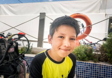 Gülümseyen beyaz çocuğun portresi. Turist otelinde dalış malzemelerinin yanında oturup tatilin tadını çıkarıyor.