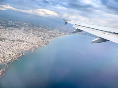 Bulutlu gökyüzüne karşı deniz manzarası ve deniz manzarası üzerinde uçan uçak kanadının kırpılmış görüntüsü