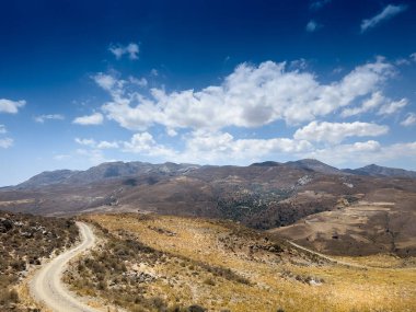 Güneşli bir günde bulutlu gökyüzüne karşı dönük yol ve görkemli dağ sıraları.