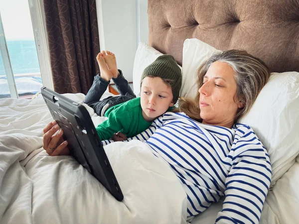 白种人的中年母亲 带着可爱的儿子在家里休息的同时 在数码平板电脑上看电影 — 图库照片