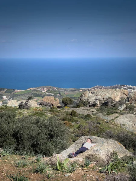晴れた日には山の上の岩の形成にリラックスした少年は 背景に海の牧歌的な景色 — ストック写真