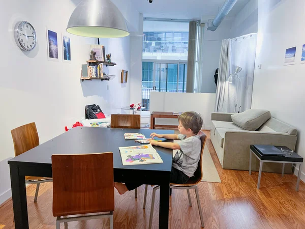 在家里客厅里 一个拿着彩色铅笔的男孩坐在餐桌前的椅子上看书 — 图库照片