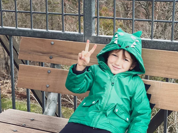 上周末坐在公园长椅上 身穿绿色冬衣的白人笑脸男孩的画像 — 图库照片