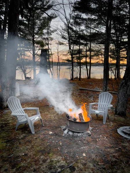 落日时 在林地的树木和湖面上燃起篝火 使椅子空无一人 — 图库照片