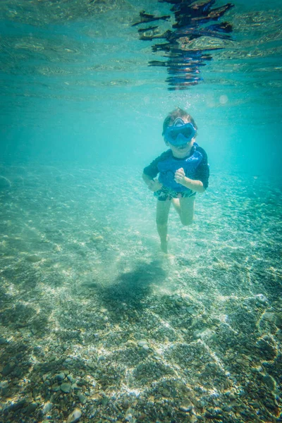 遊び心のある白人男の子の完全な長さ青いゴーグルを身に着けていると休暇中に海で水中で泳ぐ — ストック写真