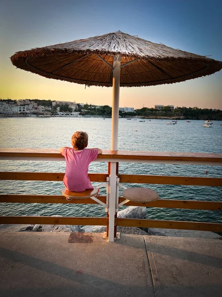 夕阳西下 白种人男孩坐在座位上 靠阳伞栏杆看海景的后视镜 — 图库照片
