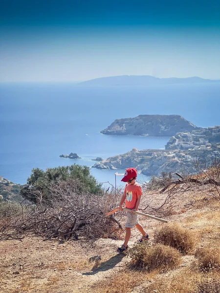 白人の少年は帽子をかぶって 晴れた日に海と空に向かって山をハイキングしている間にシャベルを運ぶ — ストック写真