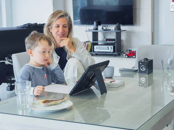 笑顔中大人母座っていますかわいいです息子E Learningスルーデジタルタブレット上のダイニングテーブルに自宅 ストック画像