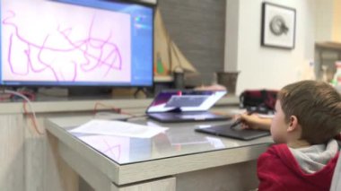 Genç çocuk masada oturuyor ve bilgisayarında dijital grafik tabletiyle çizim yapıyor. 