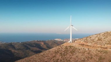 Güneşli bir günde açık mavi gökyüzüne karşı dağdaki rüzgar türbininin alçak açılı görüntüsü
