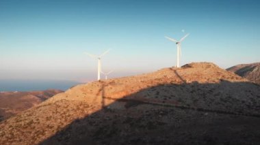 Elektrik üreten rüzgar türbinleri dağın tepesinde açık mavi gökyüzüne karşı dönüyor