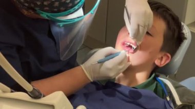 Klinikteki küçük çocuğun dişlerini inceleyen dişçi.