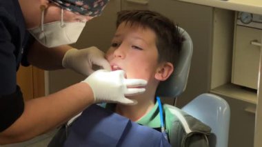 Klinikteki küçük çocuğun dişlerini inceleyen dişçi.