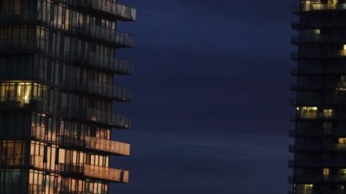 Gece boyunca mavi bulutlu gökyüzüne karşı aydınlatılmış modern gökdelenler.