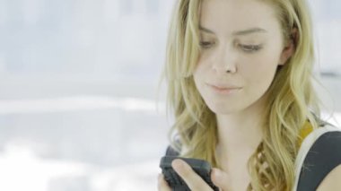 Genç sarışın kadın cep telefonu kullanıyor ve kahve içiyor.