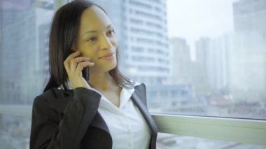 Şık takım elbiseli iş kadını panoramik pencerede akıllı telefonla konuşuyor.
