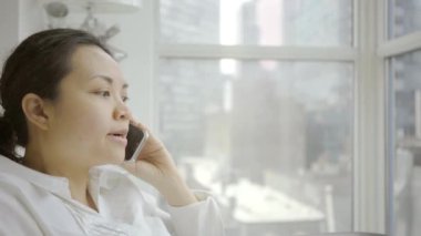 Asyalı iş kadını evde telefonla konuşuyor.