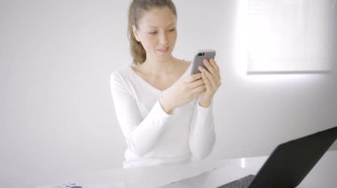 Evde dizüstü bilgisayarı ve telefonu olan beyaz bir kadın var.