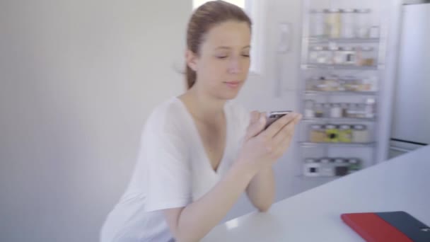 在餐桌旁的现代厨房里使用智能手机的女人 — 图库视频影像