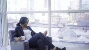 Modern ofis içi molasında koltukta oturan, kahve içip sohbet eden siyah bir iş kadını.