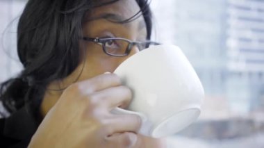 Modern ofis içinde kahve içen ve akıllı telefonla konuşan siyahi bir iş kadını.