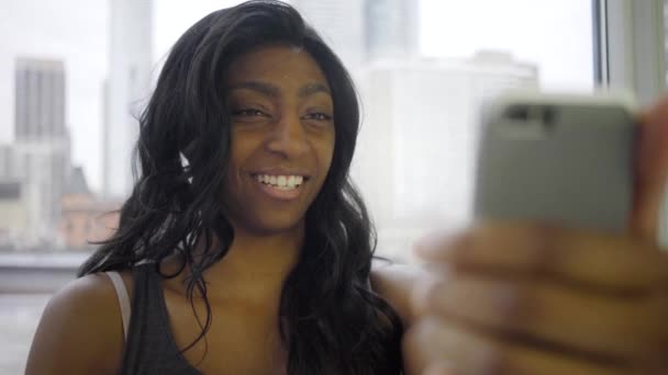 在靠近窗户的现代公寓里 漂亮的黑人女人通过智能手机聊天 — 图库视频影像