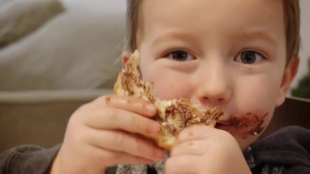 小さな男の子は自宅でチョコレートペーストでパンを食べる — ストック動画